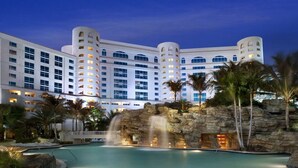 Un hotel grande con varios pisos, una fuente central y palmeras.