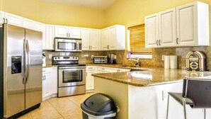 Una cocina con alacenas blancas, electrodomésticos de acero inoxidable, microondas, horno y cafetera.