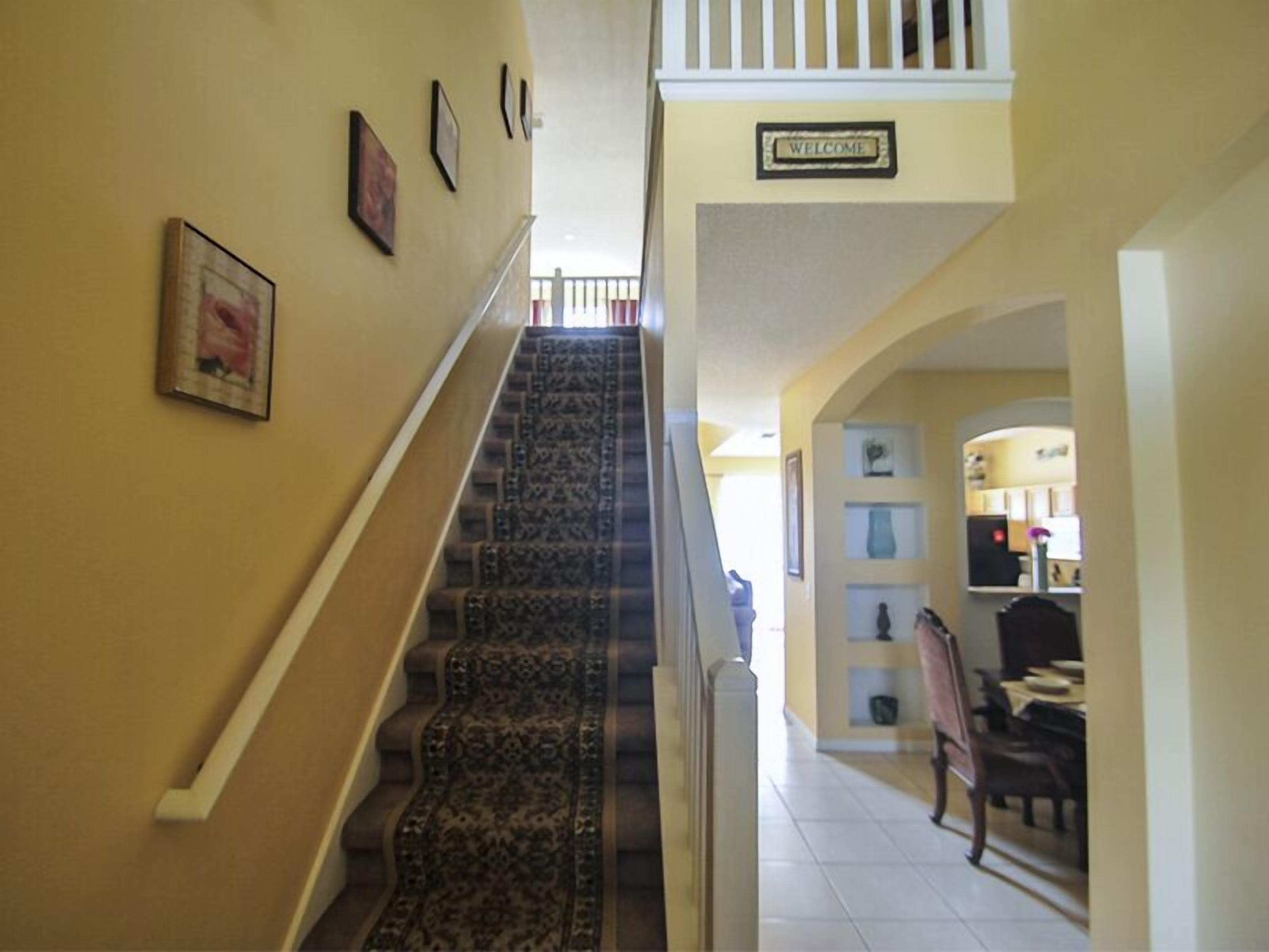 A staircase with a carpeted handrail leading to a landing with a 'Welcome' sign.