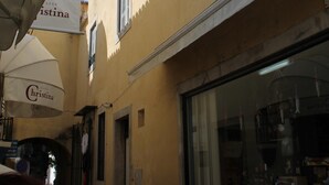 Eine enge Straße mit einem gelben Gebäude, das ein großes Fenster und ein Schild mit dem Schriftzug "Cristina" zeigt.