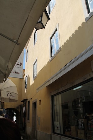 A narrow street with a yellow building featuring a large window and a sign that reads "Cristina."
