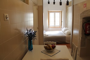 A hotel room with a bed, a window, a vase with flowers, and a bowl of fruit on the table.