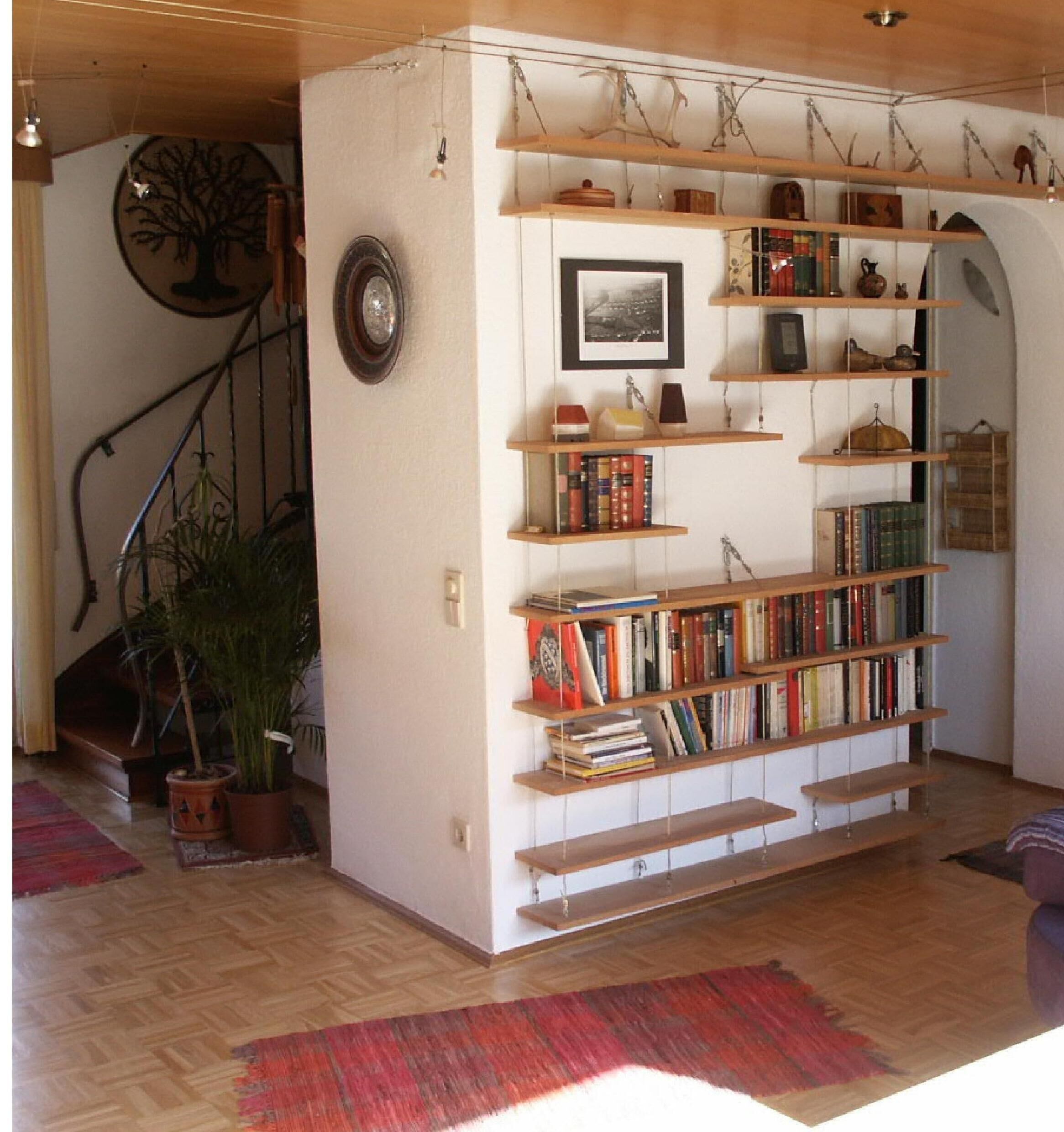 A room with a wooden bookshelf filled with books, a framed picture on the wall, and a staircase with a decorative tree.