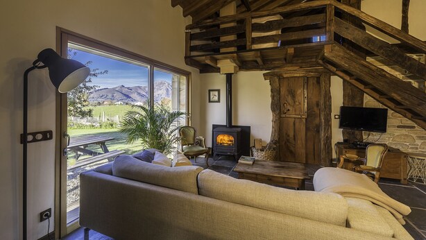 A cozy living room with a sofa, a table, a lamp, a fireplace, and a view of mountains through a large window. - Sheepfold in the village of Sare (Sare)