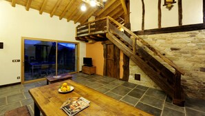 A wooden dining table with a plate of lemons and a magazine, a staircase with a stone wall, and a large window with a view of the outside. - Sheepfold in the village of Sare (Sare)
