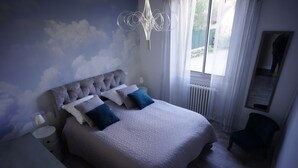 Un dormitorio con una cama grande, una mesita de noche, una silla y una ventana con cortinas.
