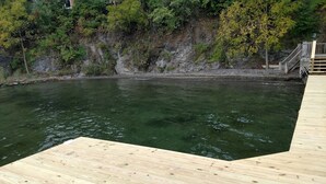 Un muelle de madera se adentra en un cuerpo de agua, con un risco rocoso y una vegetación densa al fondo.