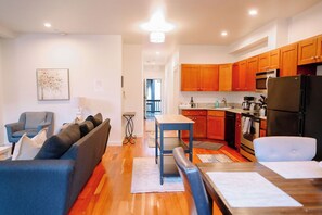 Uma sala de estar moderna com sofá, mesa de jantar e cozinha com armários e eletrodomésticos de madeira.