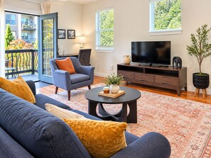 Una sala moderna con un sofá, un sillón, una mesa de centro y un televisor sobre un mueble de madera.