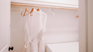 A white bathroom with a wooden towel rack holding a white bathrobe and a towel.