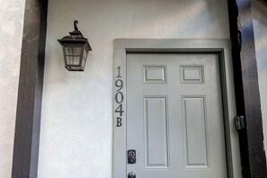 Une porte blanche portant le numéro 1904B, une bande de métal noire et un luminaire fixé au mur.