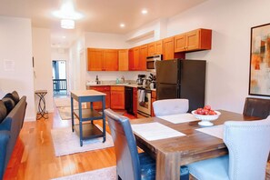 Une cuisine moderne avec des meubles en bois, un réfrigérateur noir et un coin repas comprenant une table et des chaises.
