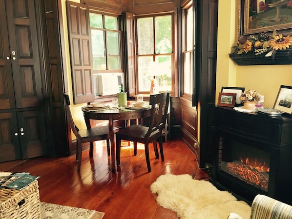 A dining area with a wooden table and chairs, a fireplace, and a window with a view of greenery.