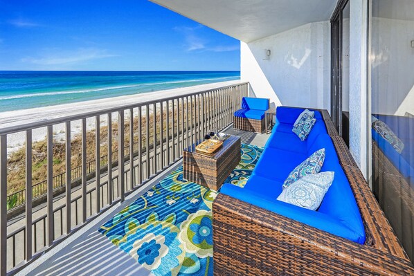 A balcony with wicker furniture, a patterned rug, and a view of the beach and ocean.
