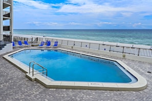 Ein Pool mit Blick auf den Ozean, blaue Liegestühle und ein Gebäude mit Balkonen.