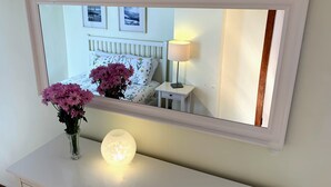 Une chambre à coucher avec un lit, une table de chevet, une lampe et un miroir posé sur une commode.
