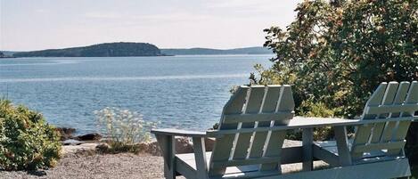 Two Adirondack chairs facing a lake with a distant island.