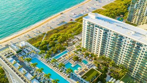 An aerial view of a resort with multiple swimming pools, a beach, and high-rise buildings.