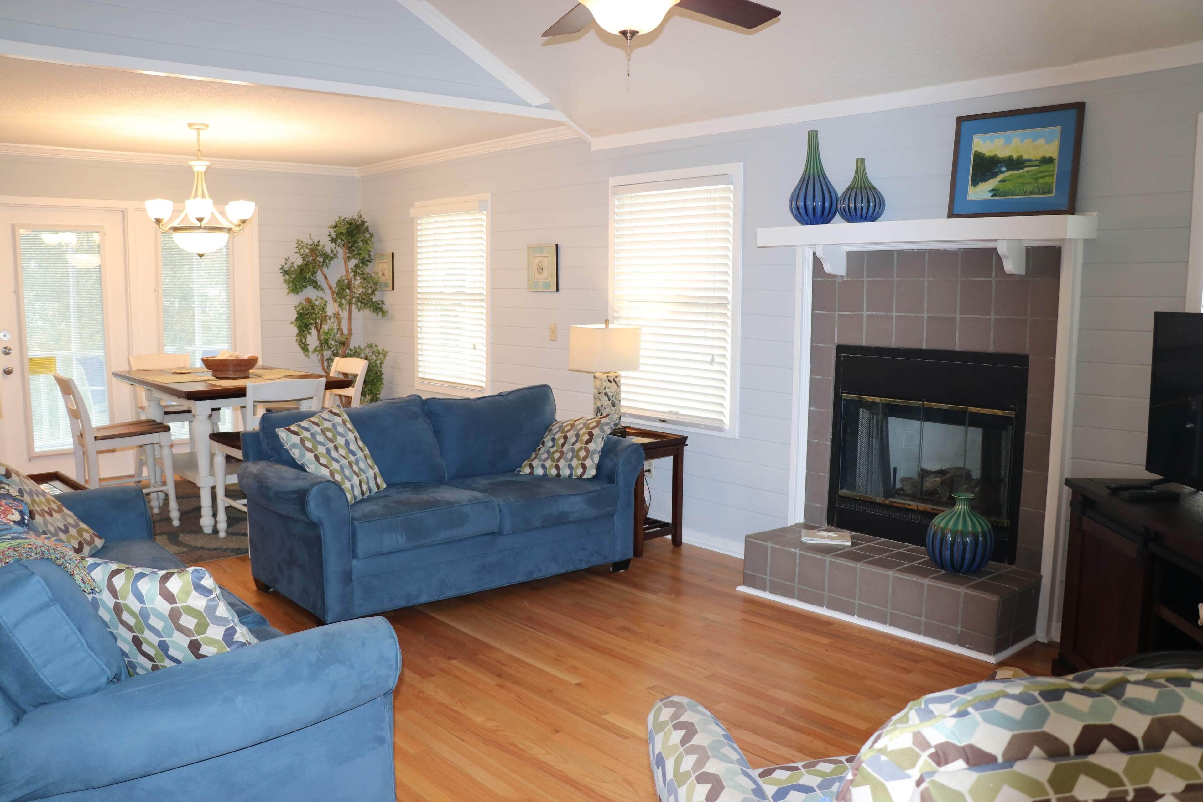 A living room with a fireplace, blue sofas, and a dining area with a table and chairs.
