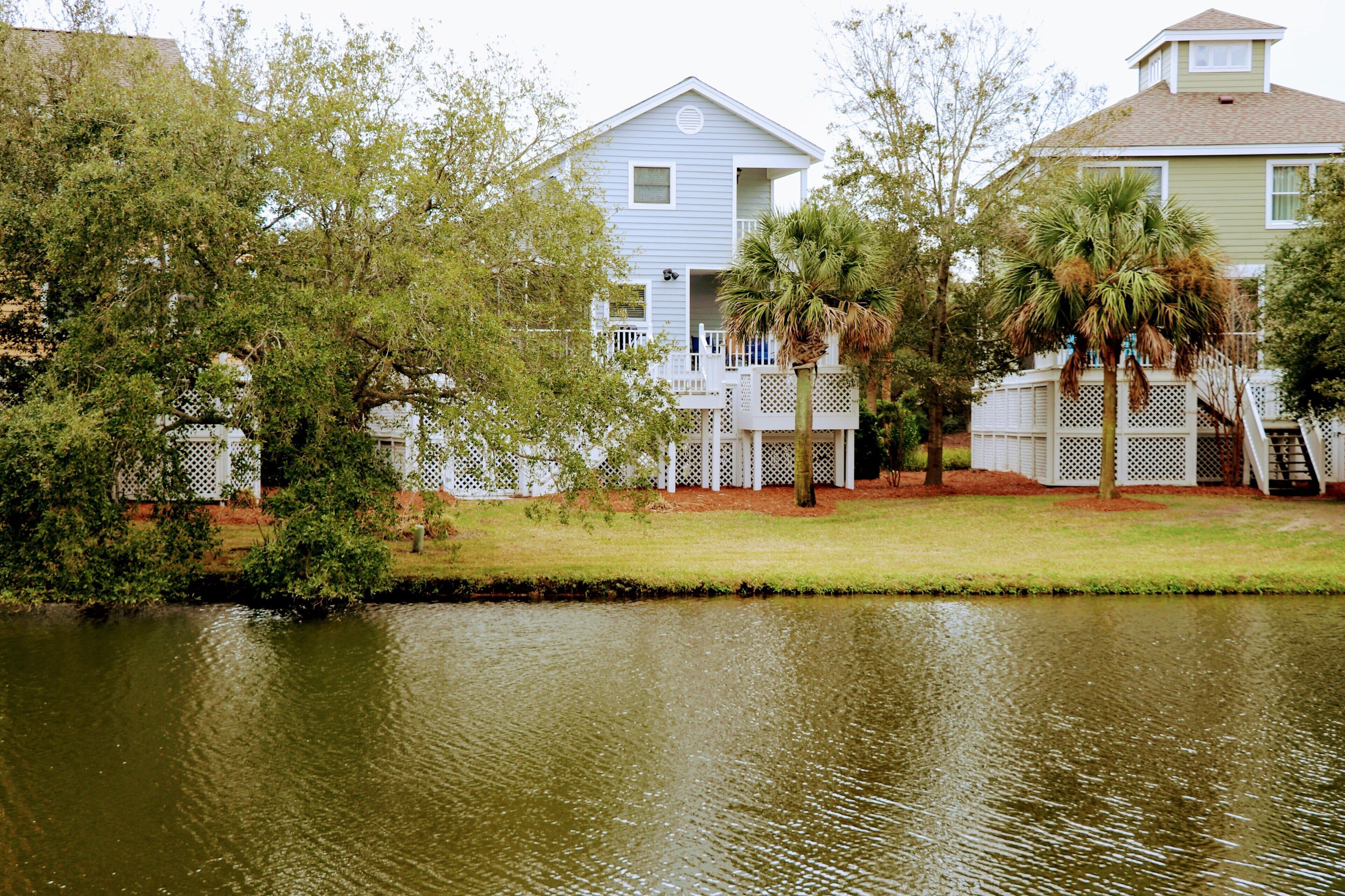 A waterfront property with a house featuring a balcony, a small deck, and a palm tree.