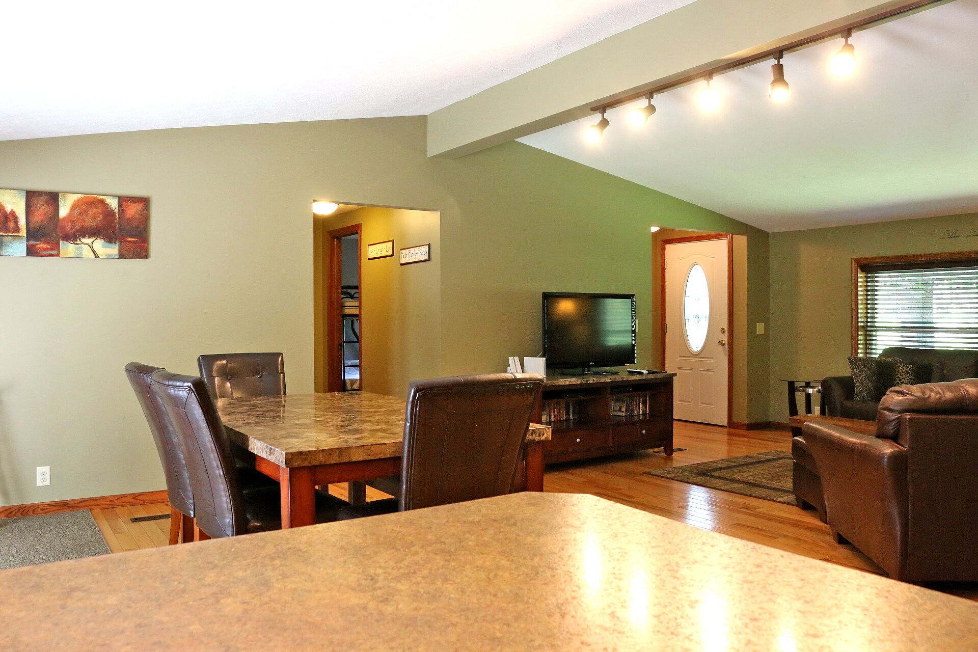 A living room with a dining area, a television, and a door leading to another room.