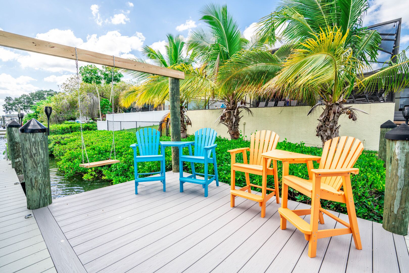 Una terraza de madera con mobiliario exterior y una hamaca, rodeada de exuberante follaje y palmeras.
