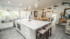 Een ruime keuken met een groot eiland, witte kasten en een eethoek met houten stoelen.
