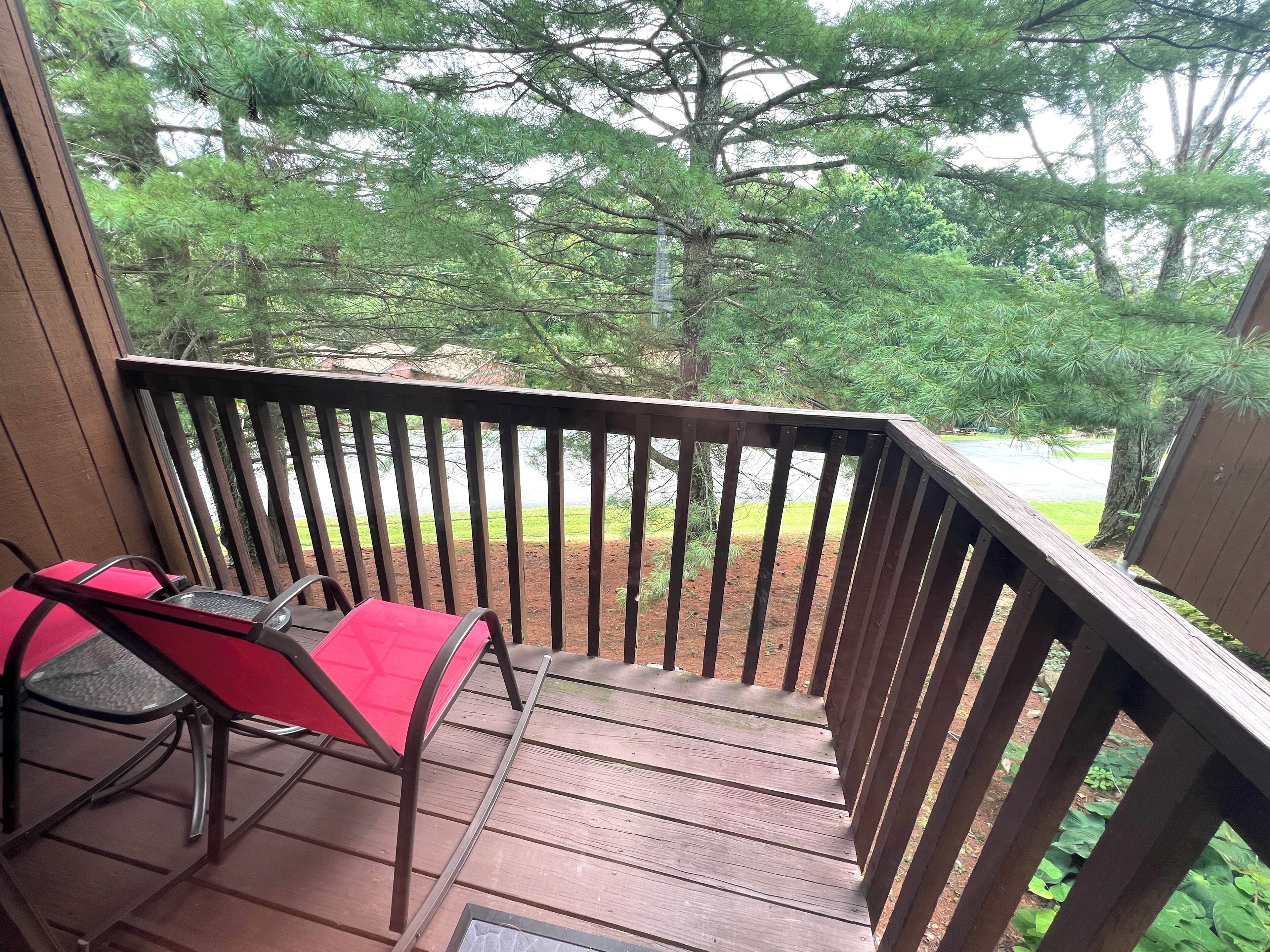 A wooden deck with a metal railing, a red chair, and a table.