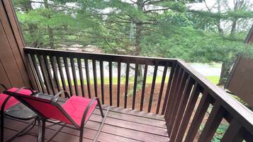 A wooden deck with a metal railing, a red chair, and a table.