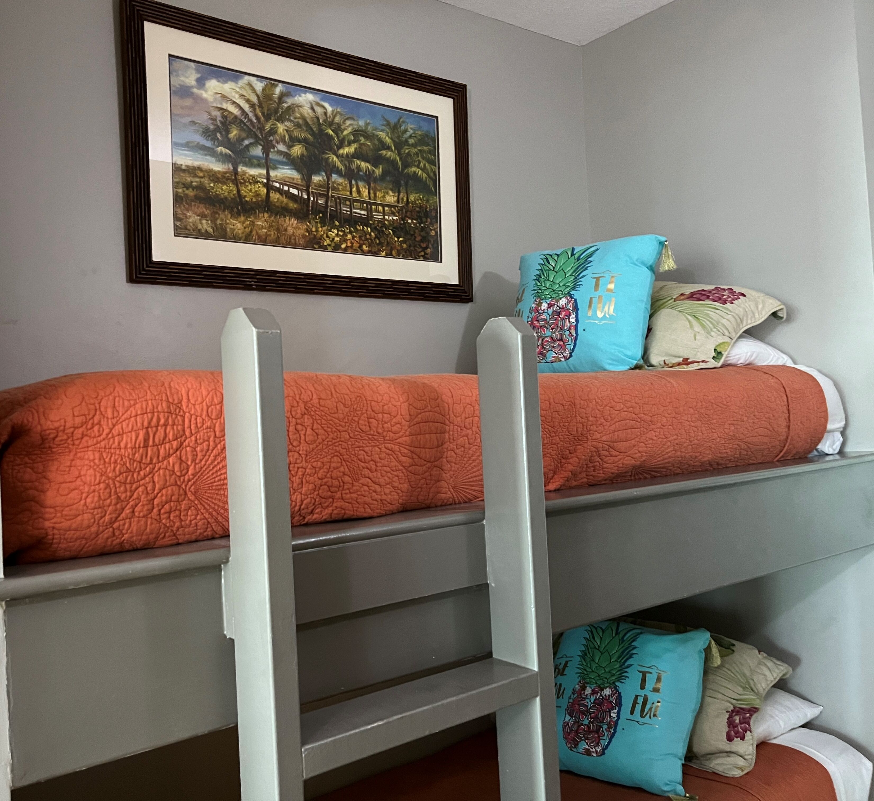 A bunk bed with a ladder, a framed picture on the wall, and a pillow with a pineapple design.