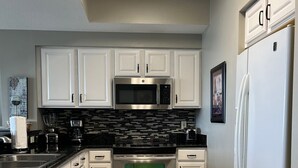 A modern kitchen with white cabinets, stainless steel appliances, and a tiled floor.