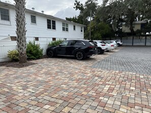 Un estacionamiento con un camino pavimentado, un edificio blanco y varios autos estacionados.