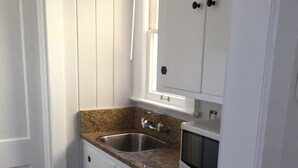 A compact kitchen with white cabinetry, a granite countertop, a stainless steel sink, and a microwave. - C6, Romantic apartment in city center, Flagler location, near beaches, parking! (St Augustine)