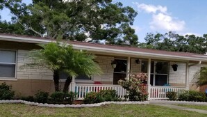 A single-story house with a front porch, a small garden, and a large tree.