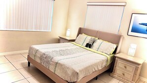 A bedroom with a large bed, two bedside tables, a nightstand, and a framed picture on the wall.