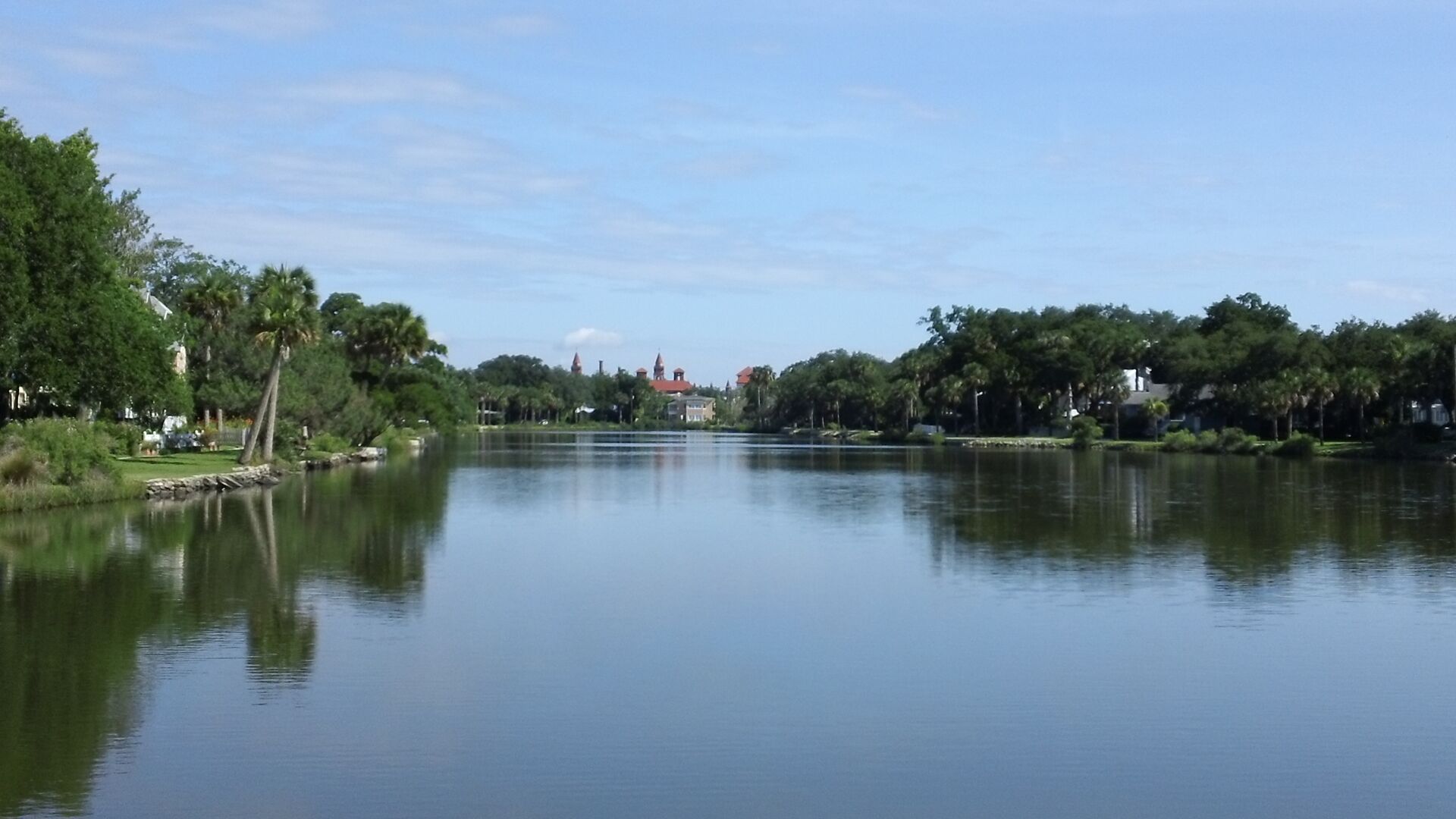 A calm lake with a distant building, surrounded by trees and greenery.