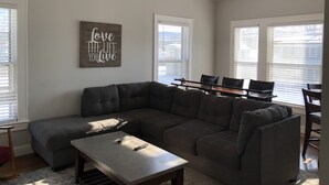 A living room with a sectional sofa, a coffee table, and a ceiling fan. There is a wall-mounted sign that reads "Love the life you live." - 1st Class Rentals Munson Manor VI at Chestnut 2nd Floor (Oneonta)