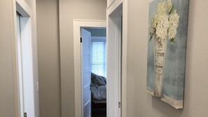 A hallway with wooden flooring, white walls, and a painting of flowers on the wall. - 1st Class Rentals Munson Manor VI at Chestnut 2nd Floor (Oneonta)