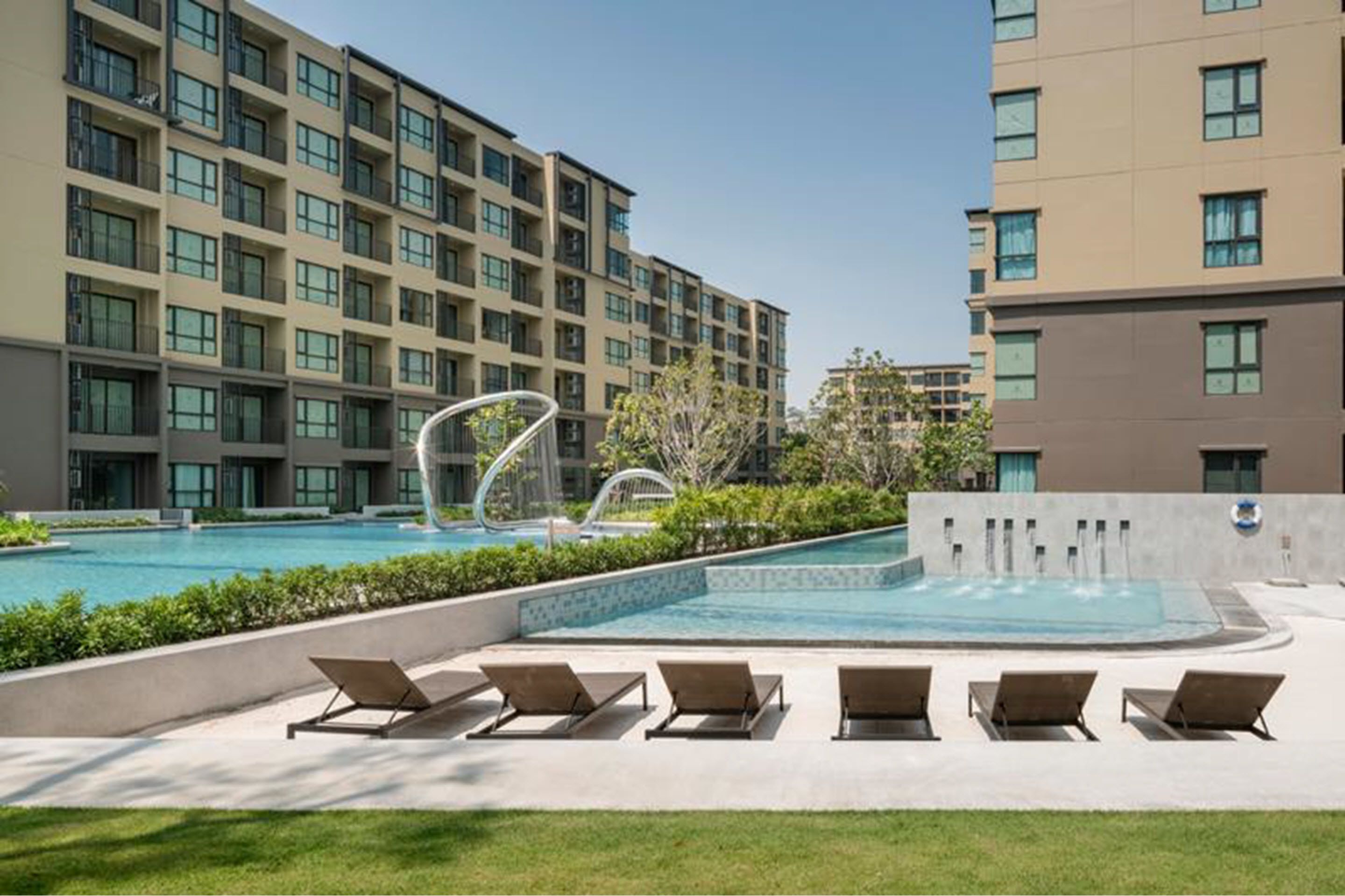 Un hotel moderno con piscina, tumbonas y un jardín paisajístico.