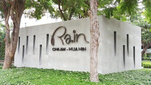 Eine Betonwand mit dem Text "Rain" und "CHAM-HUA HIN" in einer stilisierten Schrift, umgeben von Grünpflanzen.
