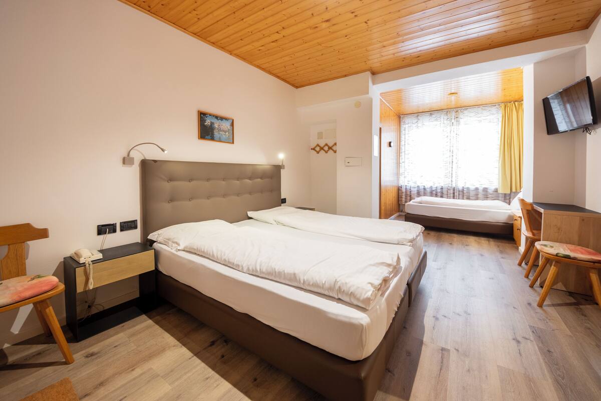 A hotel room with two beds, a desk, a chair, a television, and a window with curtains.