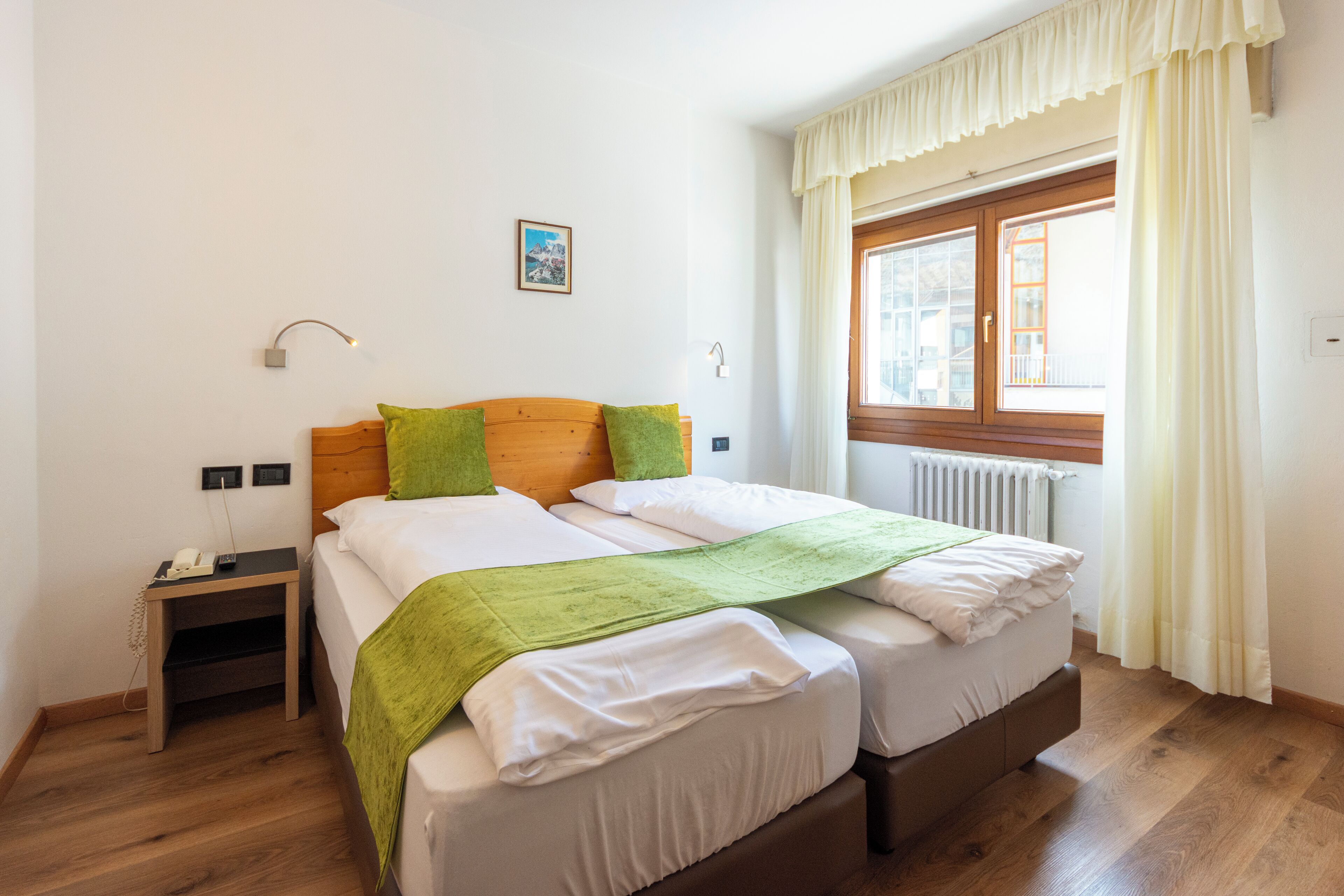 A double bed with a green throw, a bedside table with a phone, and a window with curtains.