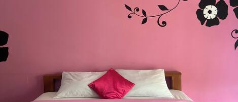 A bedroom with a pink wall, a bed with white and pink bedding, and a teal quilted bedspread.