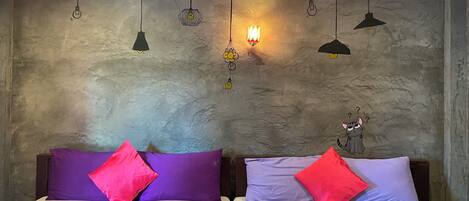 Habitación con dos camas, cada una con un edredón y almohadas de diferente color. Varias lámparas colgantes en la pared.
