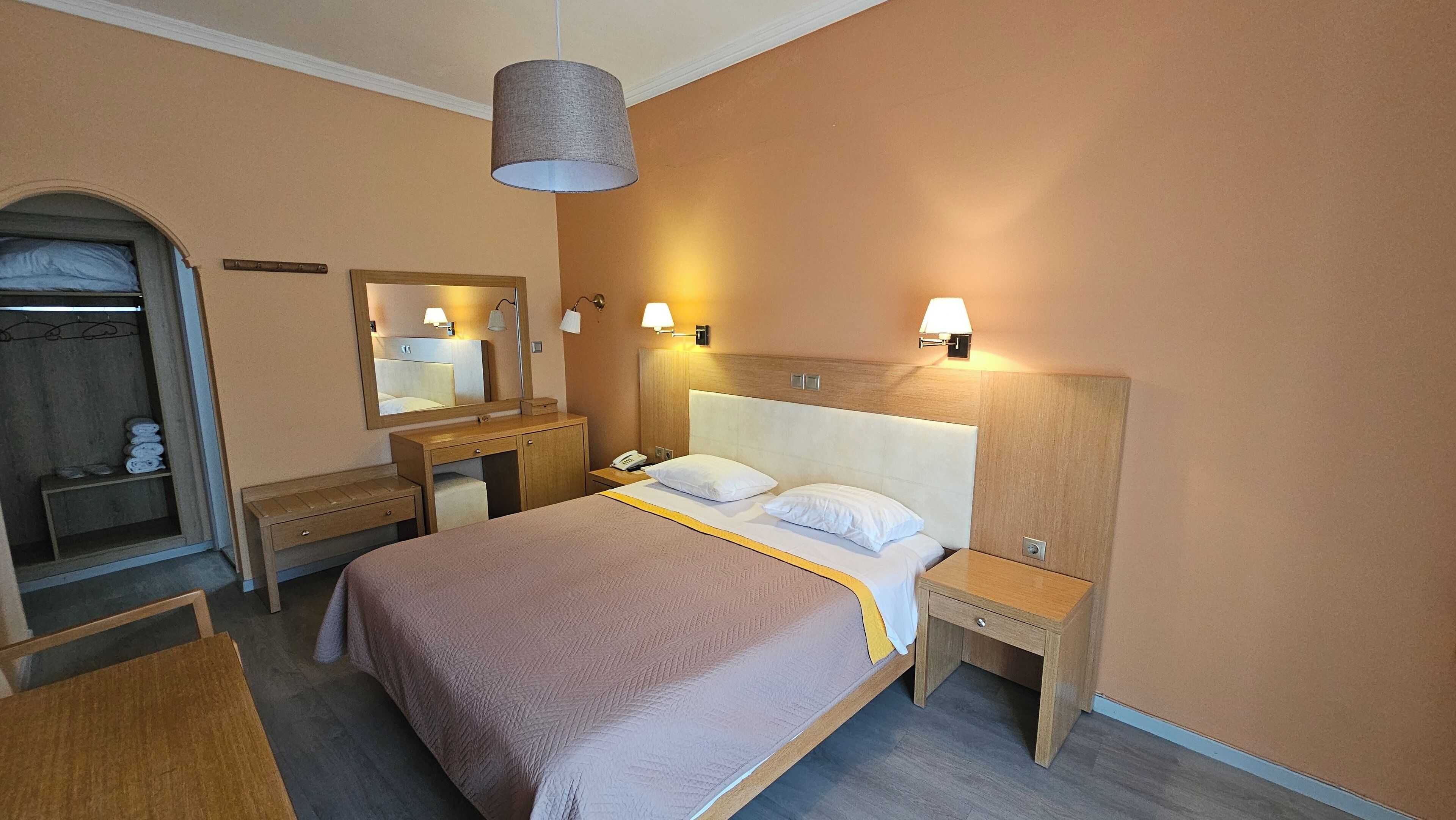 A hotel room with a bed, bedside tables, a mirror, a wardrobe, and a hanging lamp.