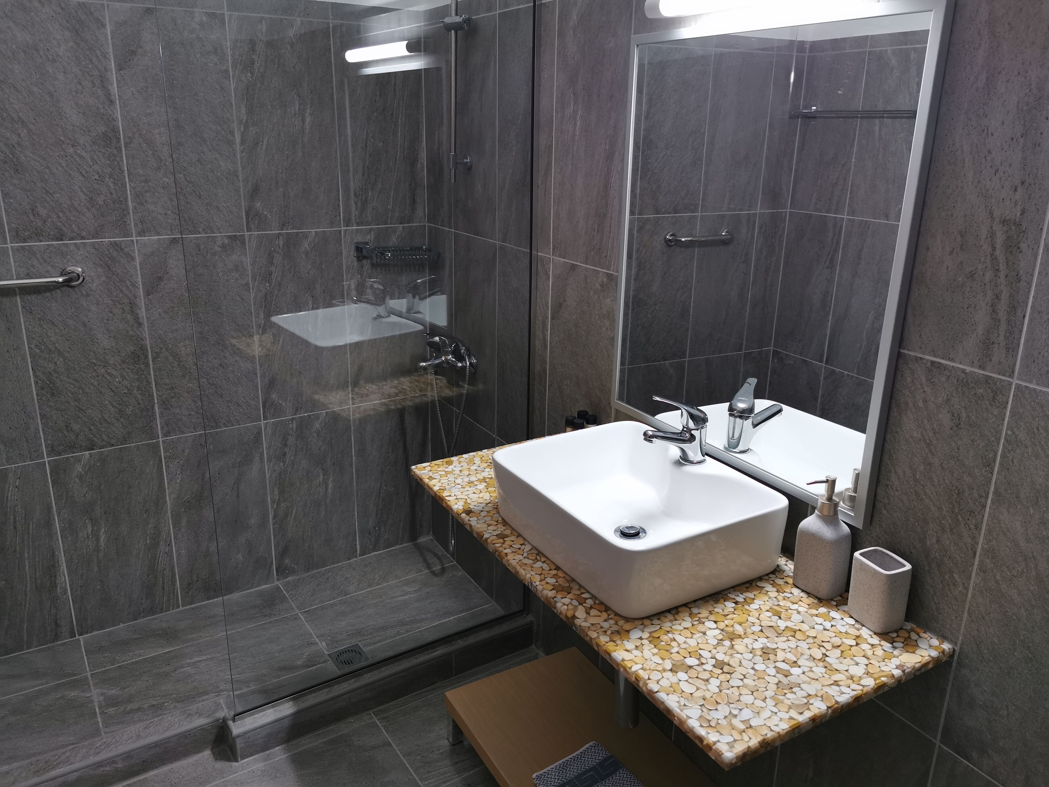 Ein modernes Badezimmer mit einer gläsernen Duschkabine, einem weißen Waschbecken mit Marmorplatte und einem großen Spiegel.