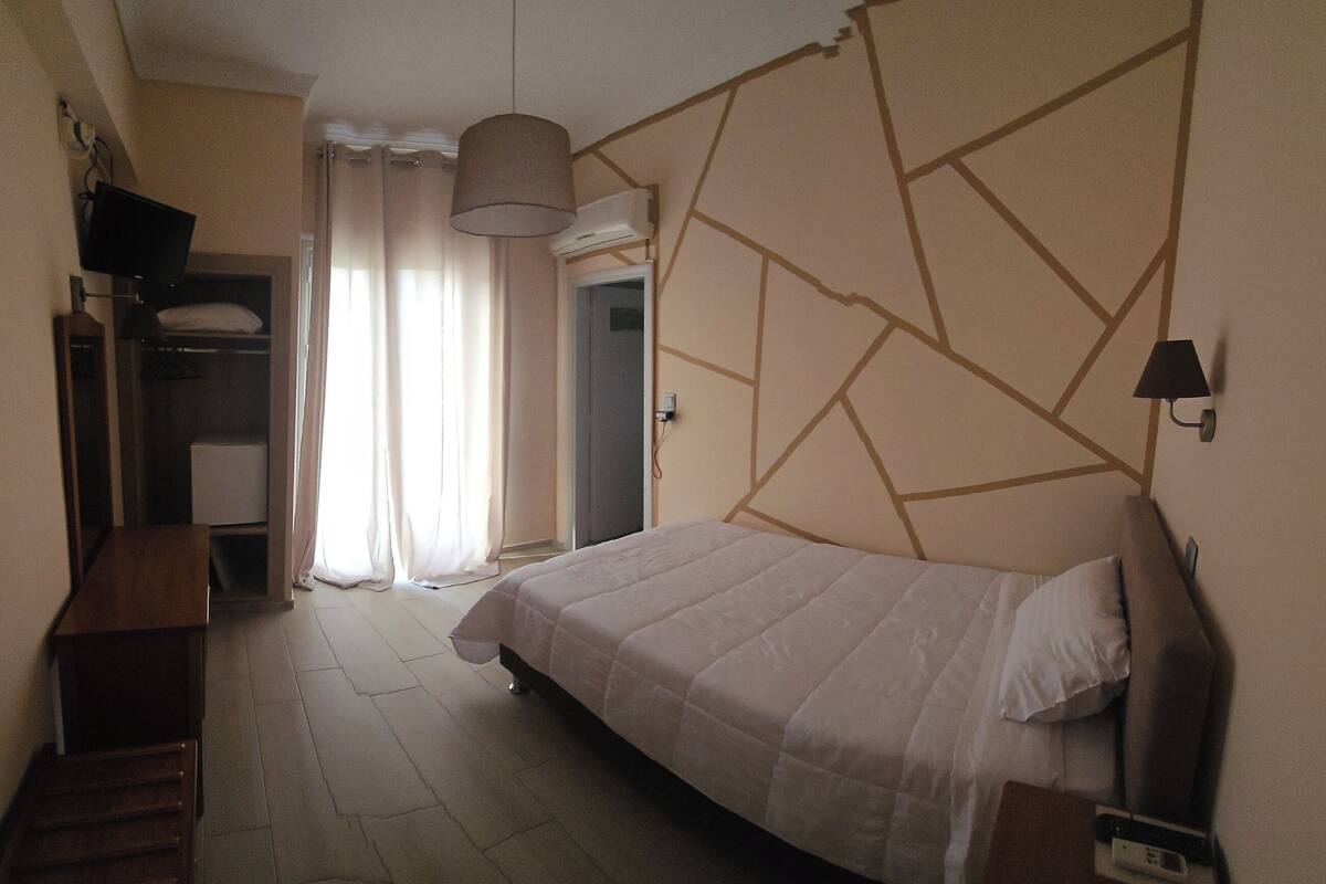 Une chambre à coucher avec un lit, une armoire, un bureau et une fenêtre avec des rideaux.