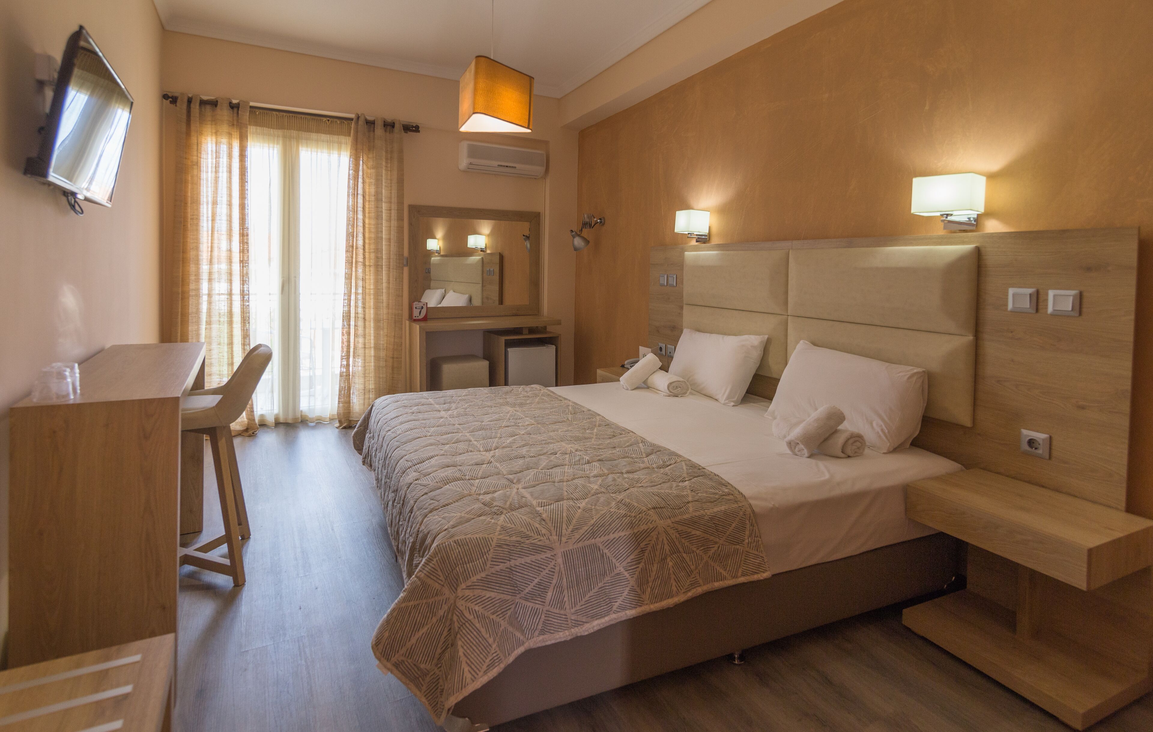 Habitación de hotel con cama, escritorio, silla y televisor en la pared.
