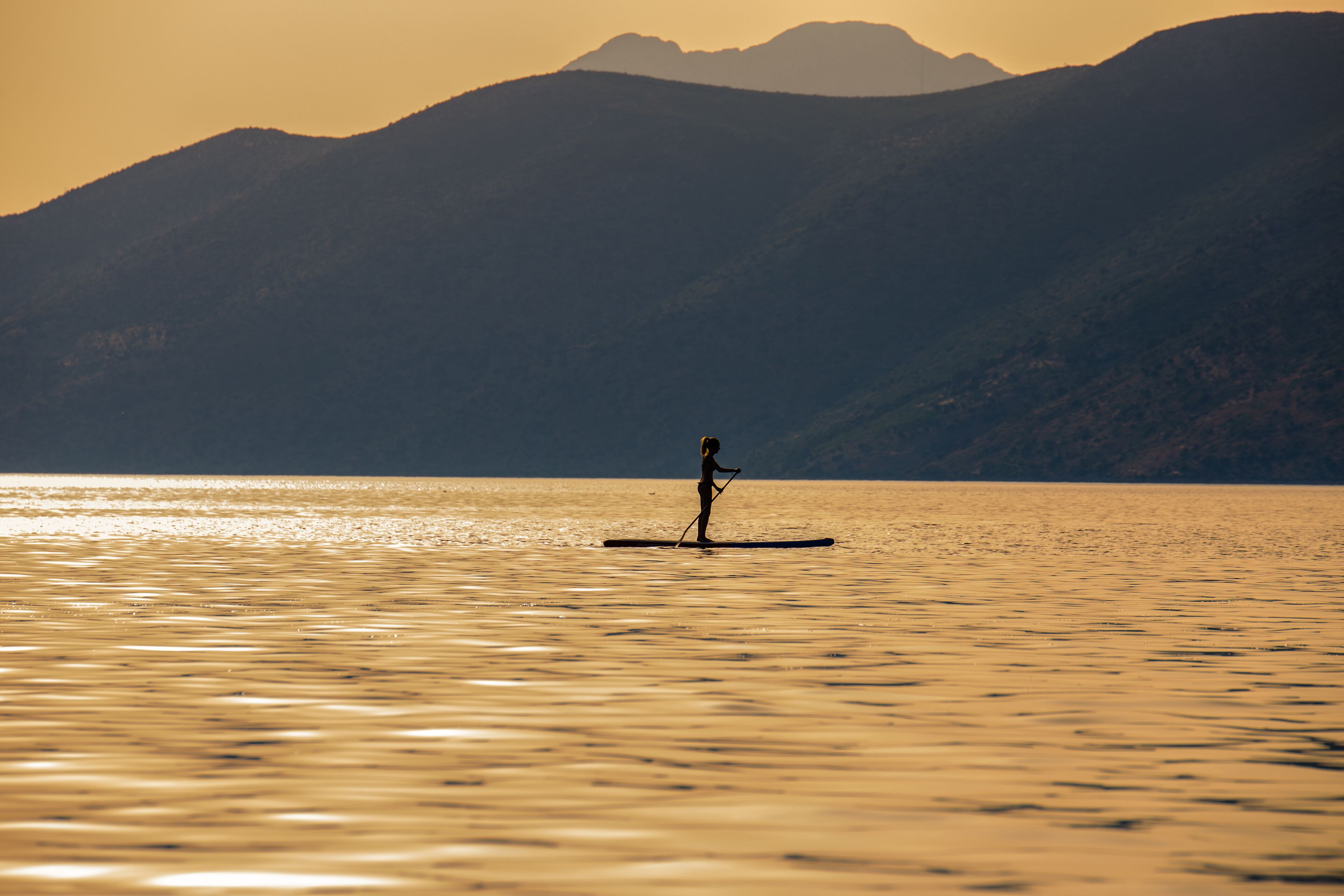A person paddleboarding on a calm body of water with mountains in the background.