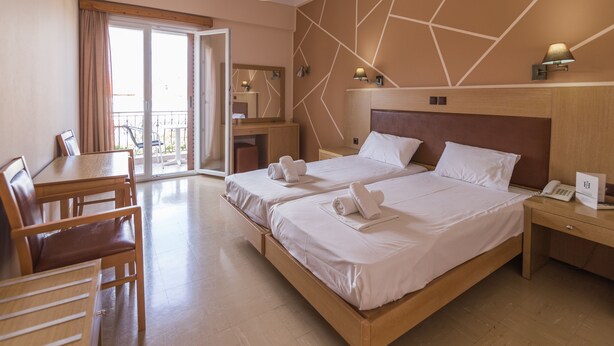 Ein Hotelzimmer mit zwei Betten, einem Schreibtisch, Stühlen, einem Balkon und einem Badezimmer.